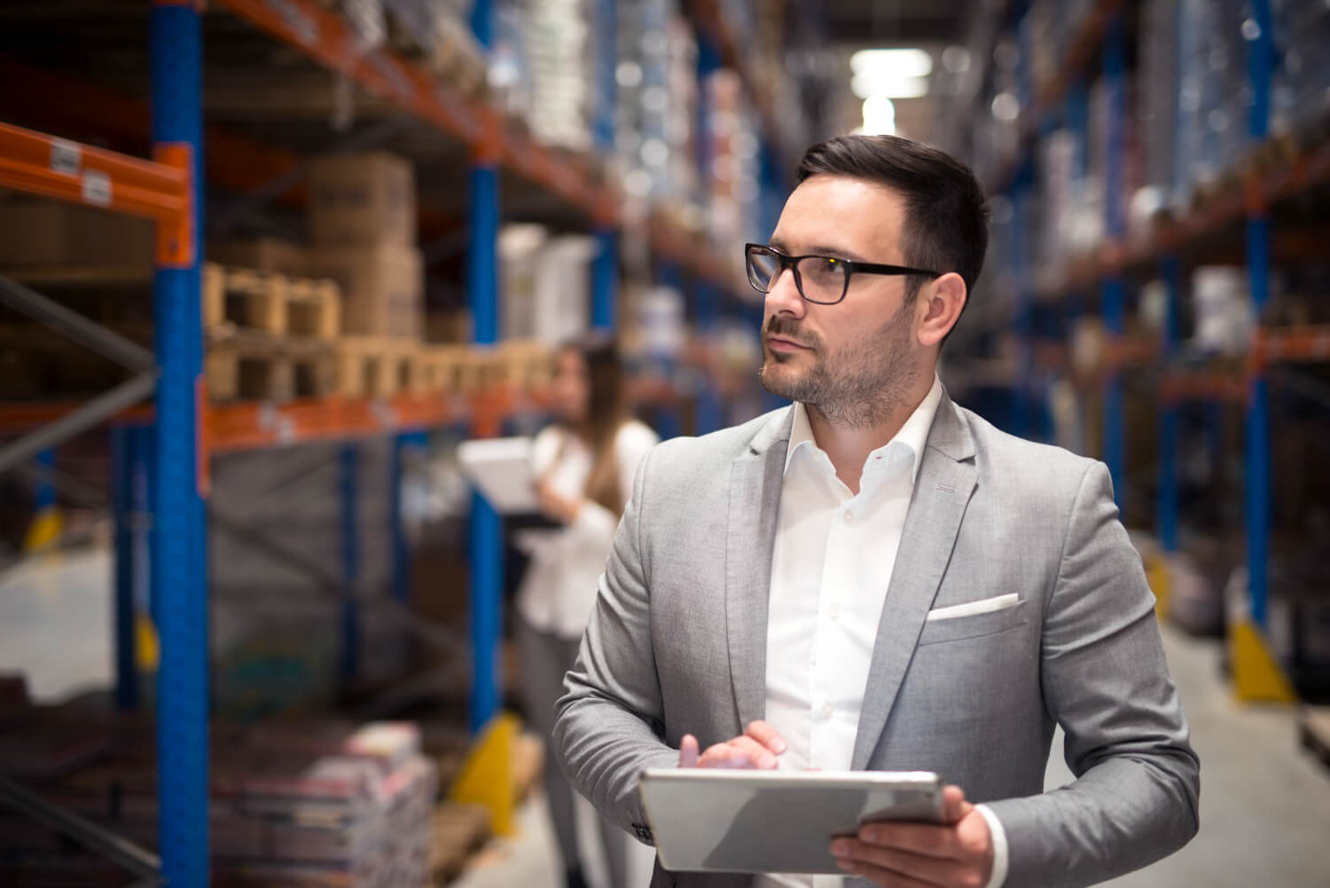 portrait successful businessman manager ceo holding tablet walking through warehouse storage area looking towards shelves